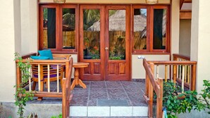 A wooden entrance with a thatched roof visible through the glass doors, a small wooden table with chairs, and a staircase leading to an upper level.