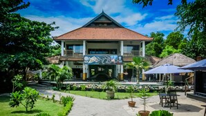 A two-story building with a tiled roof, surrounded by greenery and a pool area.