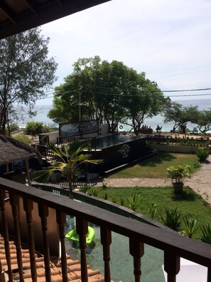 A view of a pool area with a thatched-roof structure, a signboard, and a garden with various plants. - Lutwala Dive and Bungalows (Gili Trawangan)