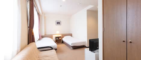 Une chambre d’hôtel avec une armoire en bois, un canapé, deux lits simples, une table de chevet avec une lampe et un téléviseur.