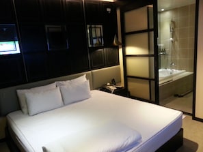 A hotel room with a large bed, a nightstand, and a bathroom visible through a glass partition.