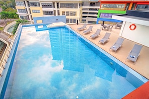 Una piscina en la azotea con sillones de descanso y un flotador salvavidas, rodeada de edificios de varios pisos.
