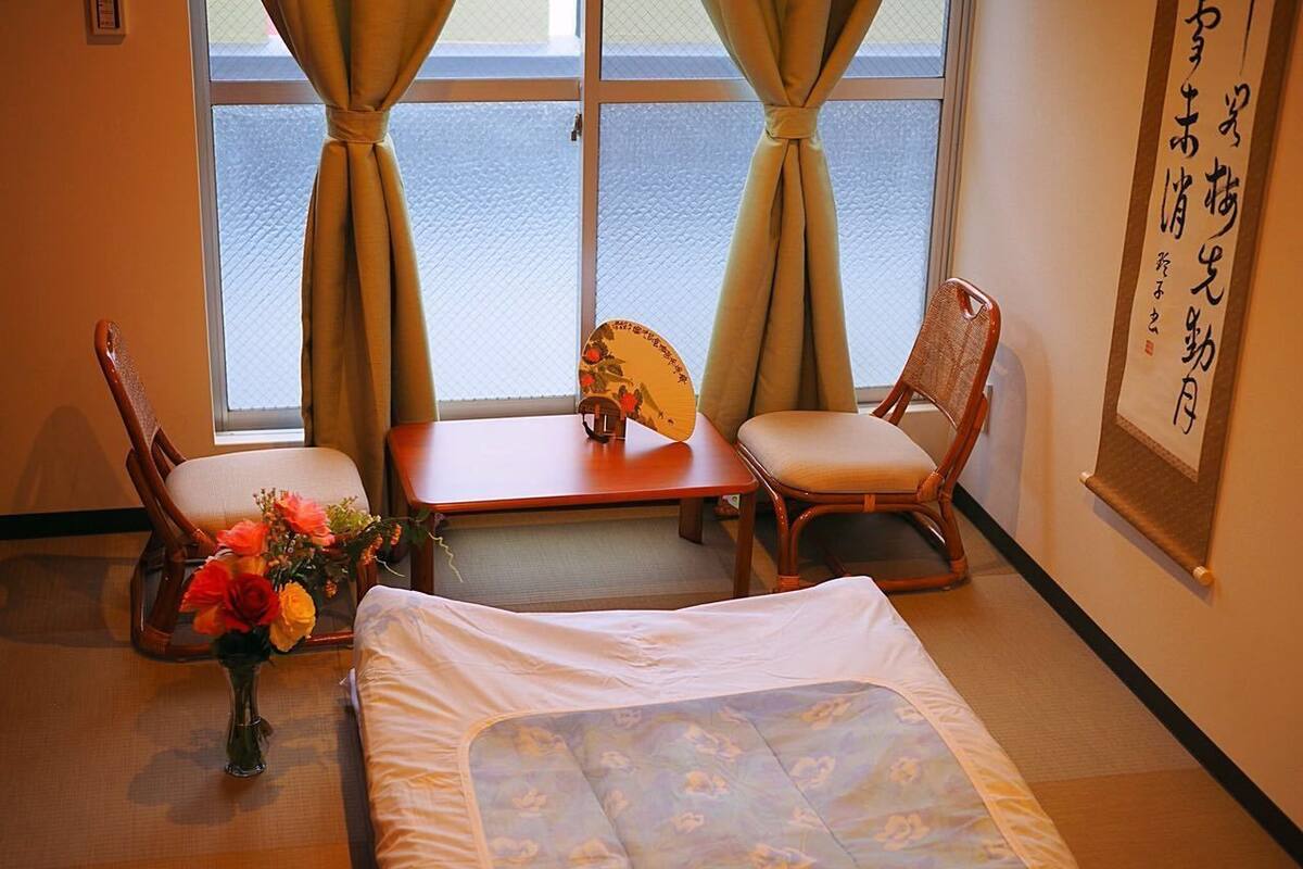 A hotel room with a bed, two chairs, a small table, and a window with curtains.
