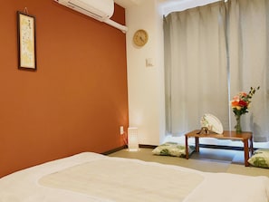 A hotel room with a bed, a bedside table with a vase of flowers, a clock on the wall, and a window with curtains. - Hotel Saikoukan (Osaka)