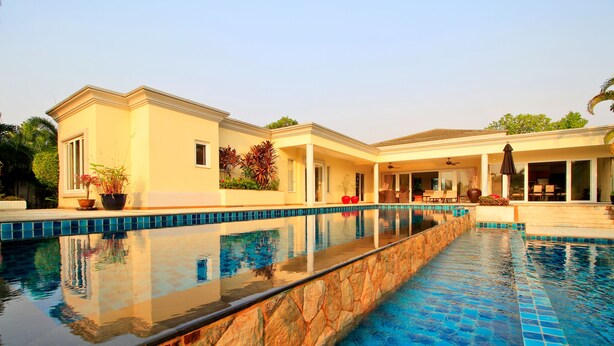 Ein Pool mit Steinbord, eine überdachte Terrasse und ein Gebäude mit großen Fenstern und einer flachen Dachkonstruktion.