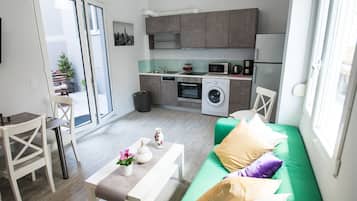 Un espace de vie compact comprenant un coin cuisine, un coin repas et un canapé vert agrémenté de coussins.
