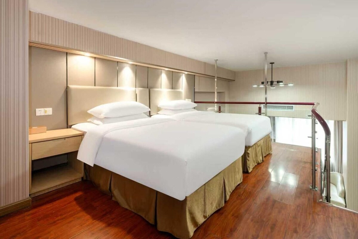 A hotel room with two beds, a wooden floor, a desk, and a mirror.