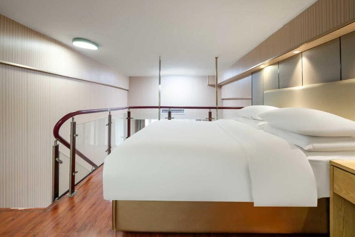 A modern hotel room with a large bed, wooden flooring, and a glass railing.