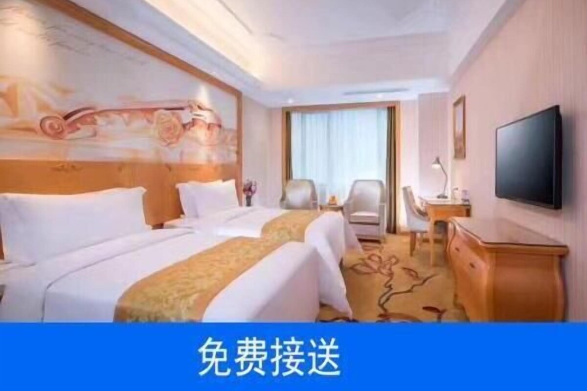 A hotel room with two beds, a desk, a chair, a television, and a painting on the wall.