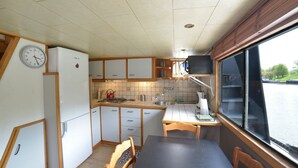 Una cocina compacta con estufa, lavamanos y armarios, una mesa de comedor con sillas y un reloj en la pared.