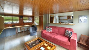 Un salón amplio con techo de madera, un sofá rojo, una mesa de centro y una cocina visible a través de una ventana.
