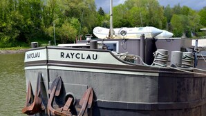 Un barco llamado “RAYCLAU” amarrado en un muelle con un paisaje boscoso de fondo.