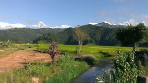 A river flowing through a rural landscape with green fields and a mountain range in the background. - Hotel Highland Comfort (Pokhara)