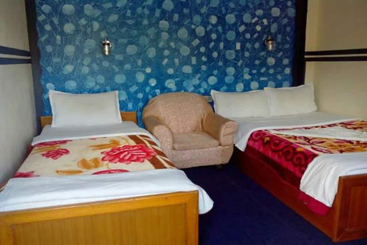 Ein Hotelzimmer mit zwei Einzelbetten, einem Sessel und einer Wand mit blauem Muster.