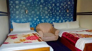 A hotel room with two beds, a chair, and a blue patterned wall. - Hotel Highland Comfort (Pokhara)