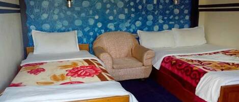 A hotel room with two beds, a chair, and a blue patterned wall.
