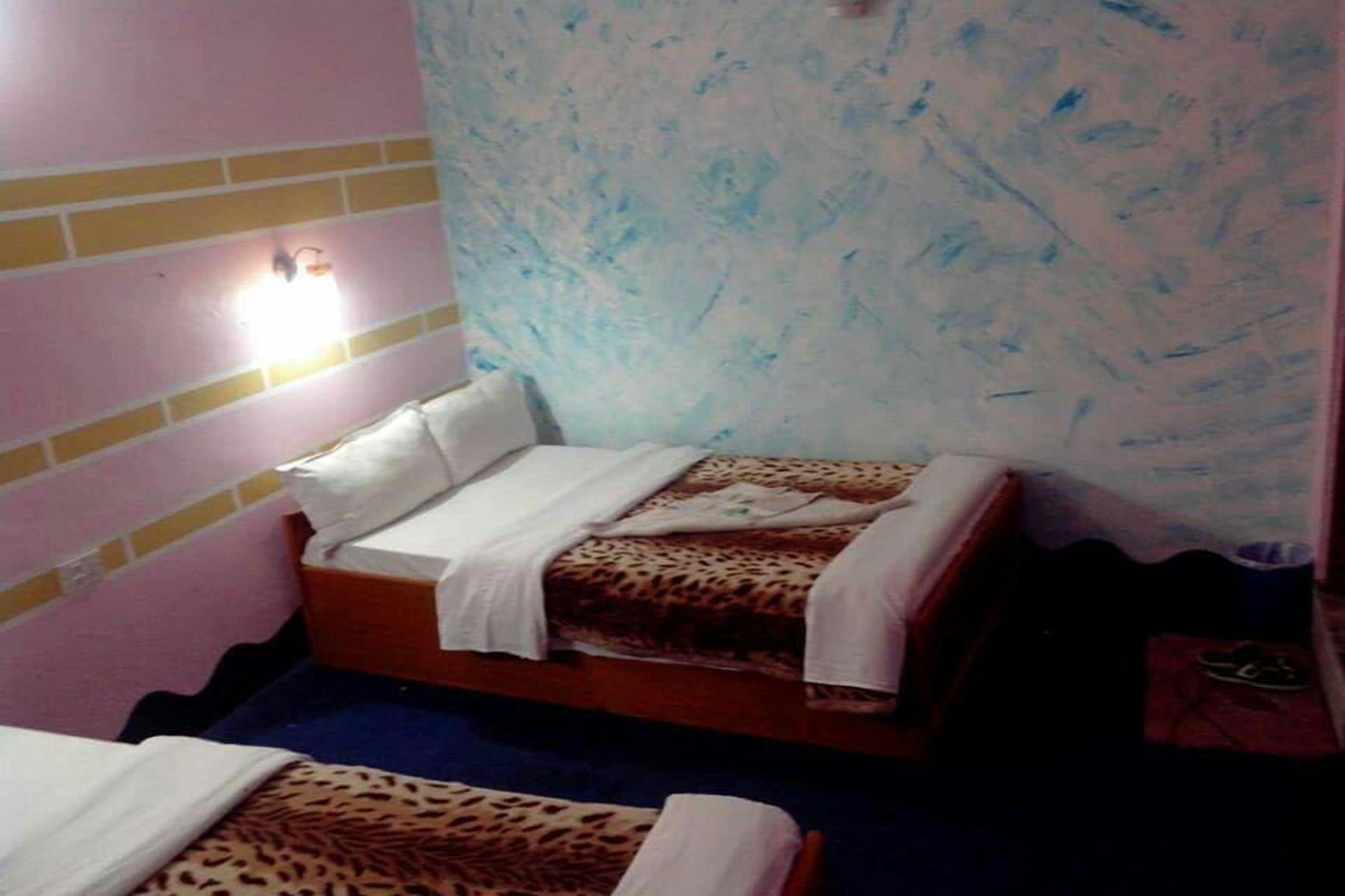 A small room with two beds, each with a leopard print bedspread. There is a wall-mounted light fixture above one bed.