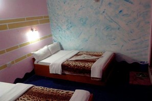 A small room with two beds, each with a leopard print bedspread. There is a wall-mounted light fixture above one bed. - Hotel Highland Comfort (Pokhara)