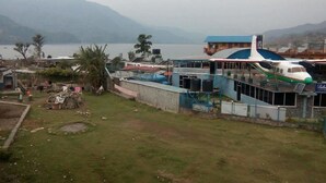 A small airport with a single airplane parked on the tarmac, surrounded by buildings and a mountainous backdrop. - Hotel Highland Comfort (Pokhara)