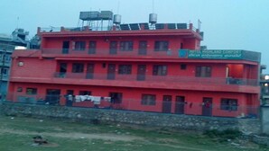 A red multi-story building with a sign for 'Hotel Highland Comfort' and a water tank on the roof. - Hotel Highland Comfort (Pokhara)
