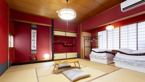 A traditional Japanese room with tatami flooring, a low wooden table, a hanging light fixture, and a stack of neatly folded bedding. - Kanazawa guesthouse nagonde - Hostel (Kanazawa)
