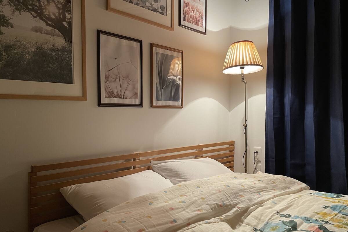 A bedroom with a wooden bed, white pillows, a floral-patterned duvet, and a standing lamp.