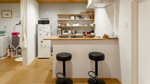 A compact kitchen with a microwave, toaster, and refrigerator. There are two stools at the counter and a TV mounted above it. - Kanazawa guesthouse nagonde - Hostel (Kanazawa)