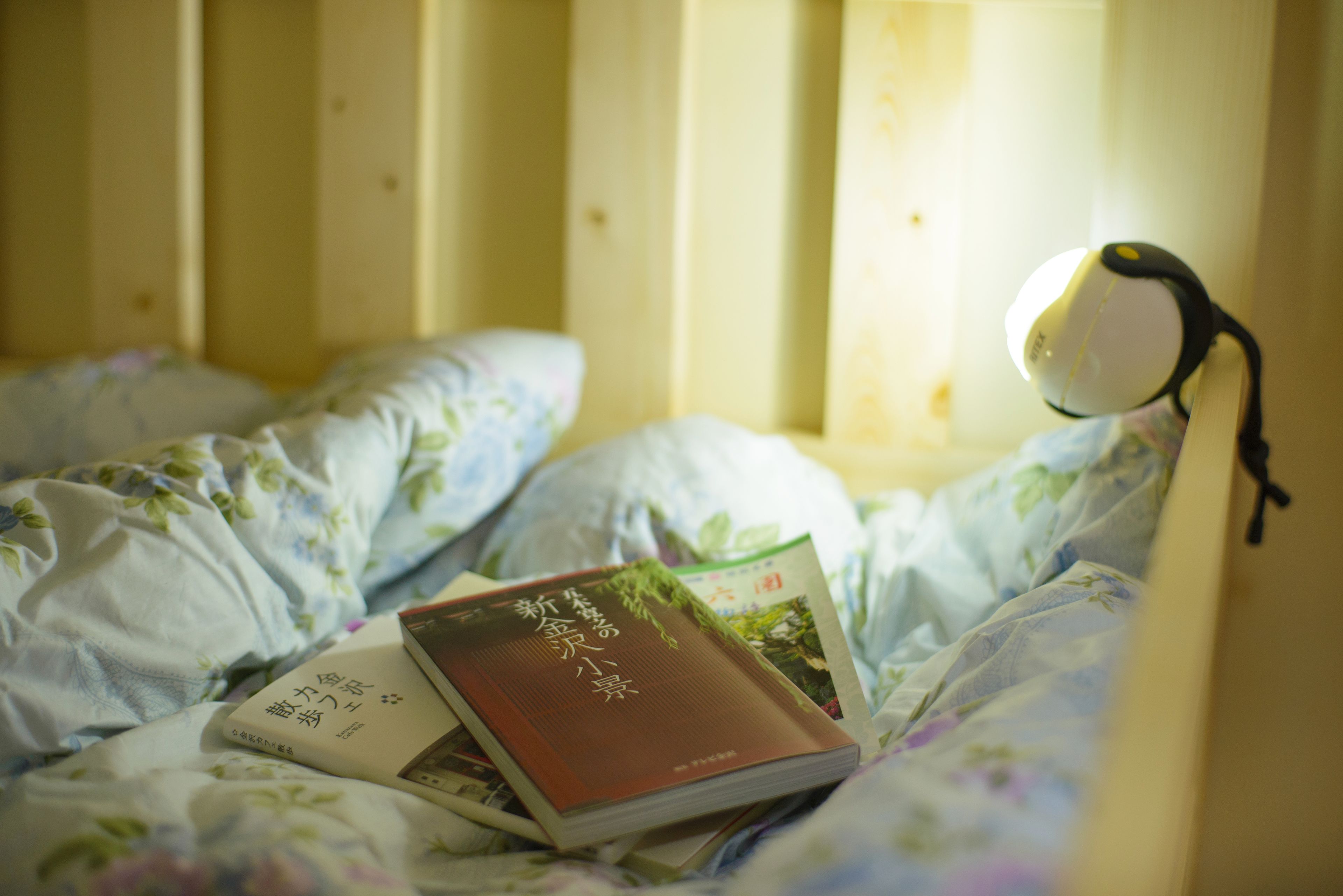 A bed with a floral comforter, a book, and a desk lamp.