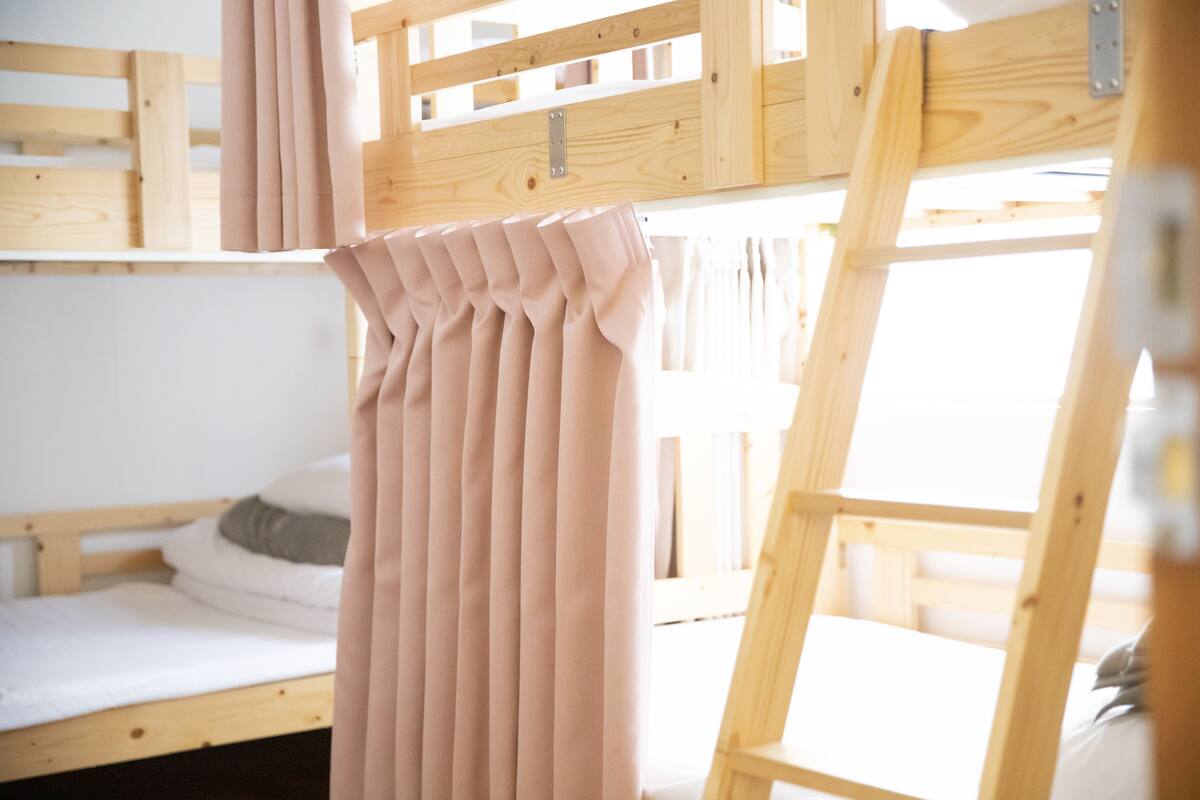 A bunk bed room with a wooden frame, a window with curtains, and a bed with white bedding.