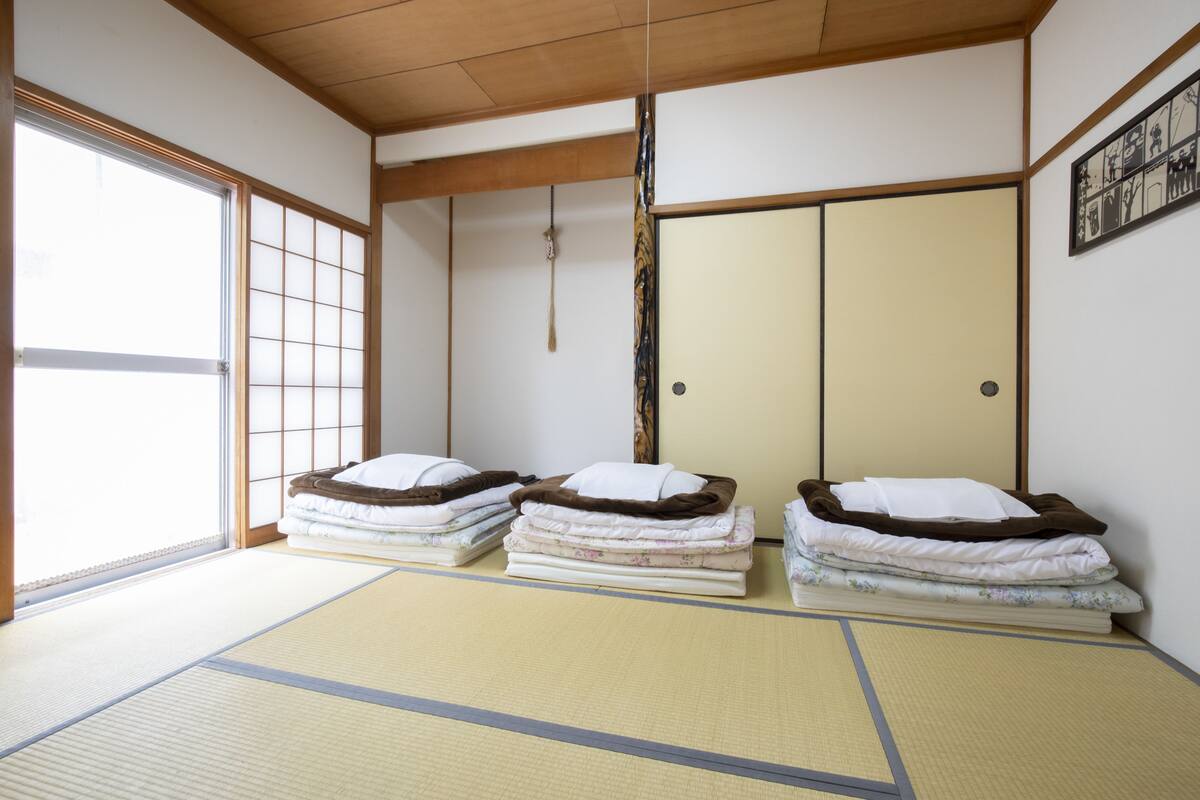 A traditional Japanese room with tatami flooring, two tatami mats, a shoji screen, a sliding door, and a framed picture on the wall.