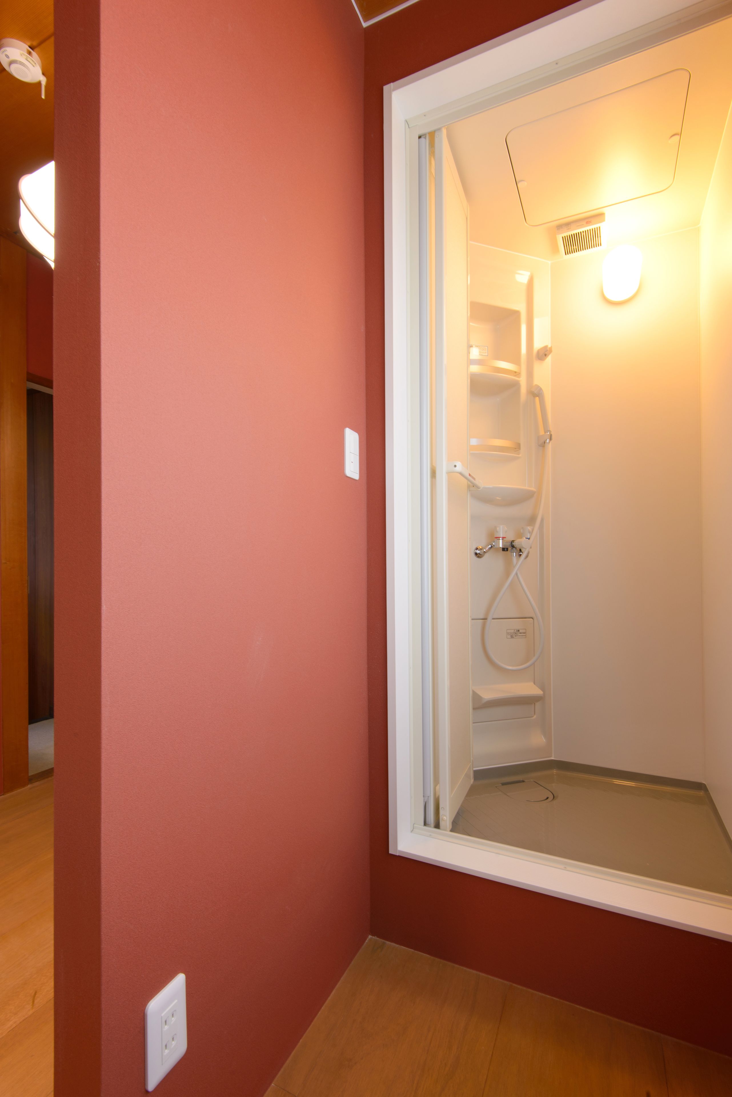 Una habitación con una pared roja, una puerta blanca que da a una zona de ducha y suelo de madera.