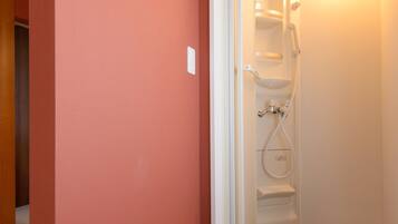 Una habitación con una pared roja, una puerta blanca que da a una zona de ducha y suelo de madera.