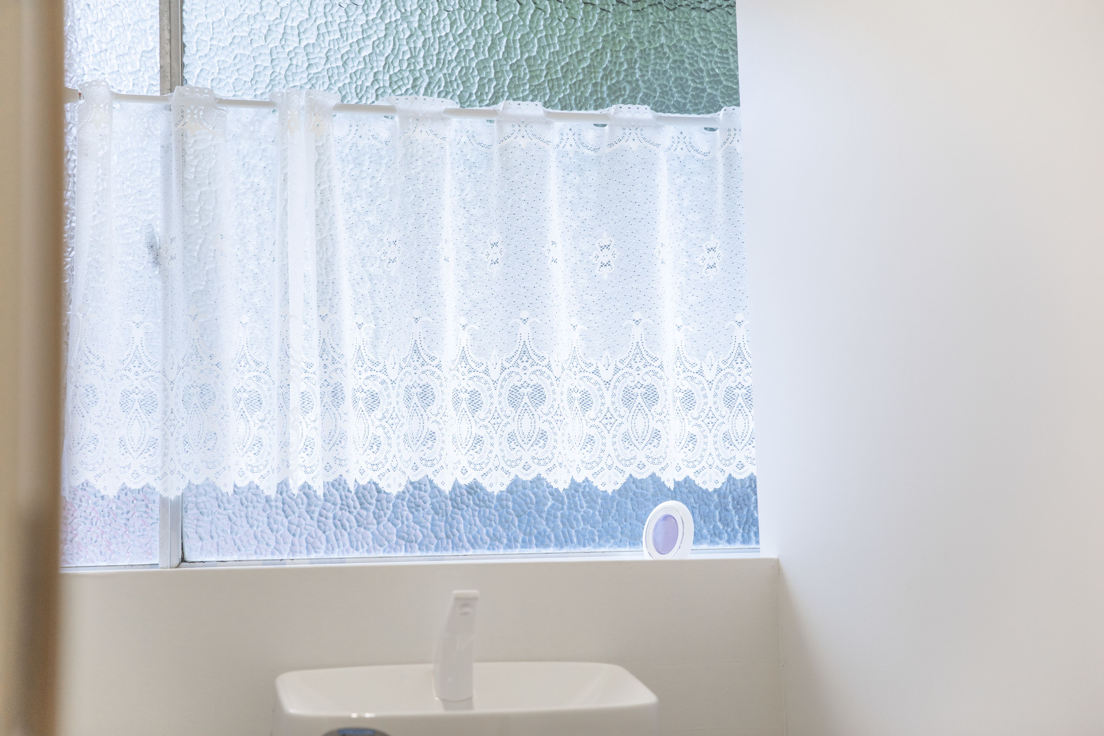 A bathroom with a white sink and a window with lace curtains.