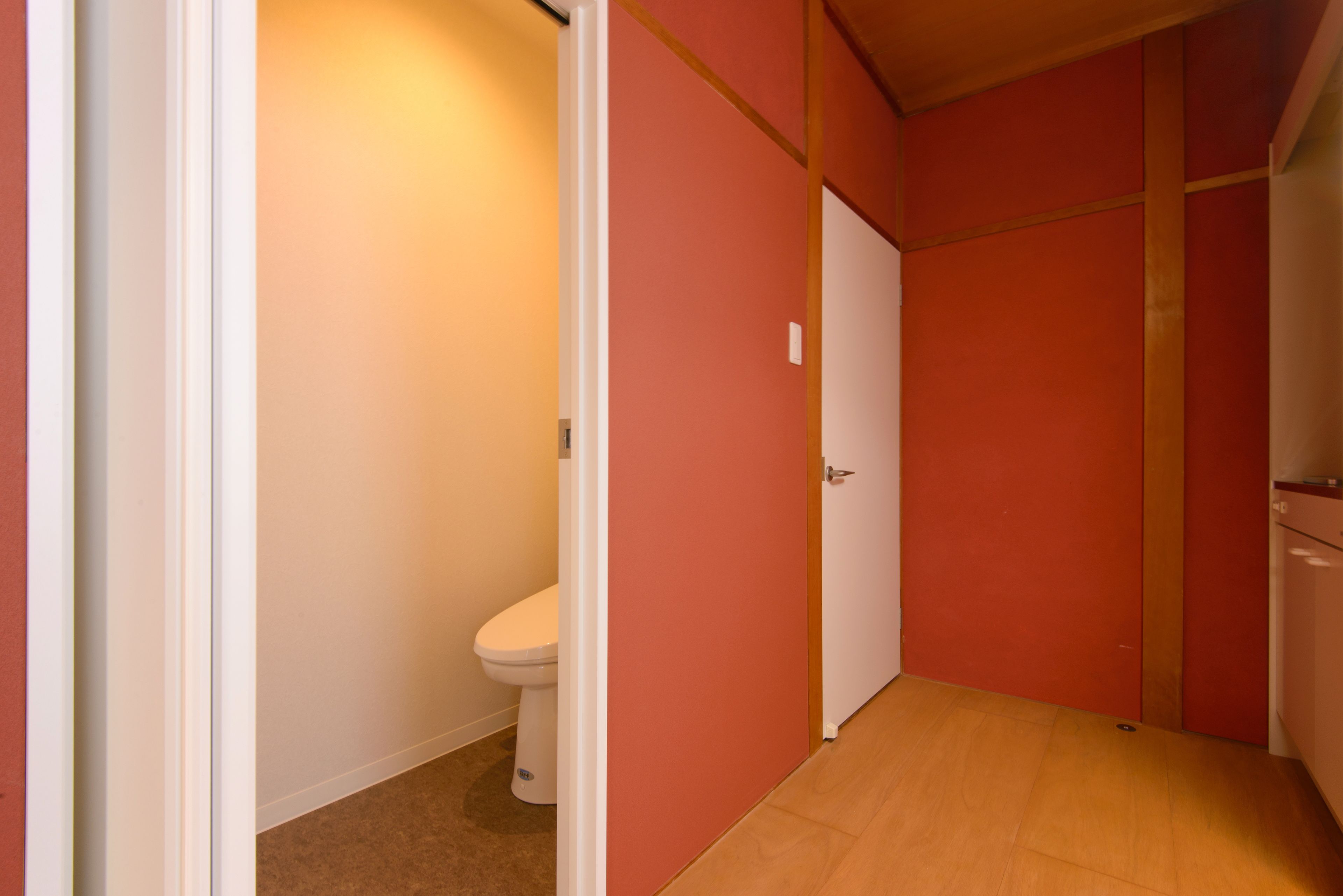 A narrow hallway with a toilet on the left and a door on the right.