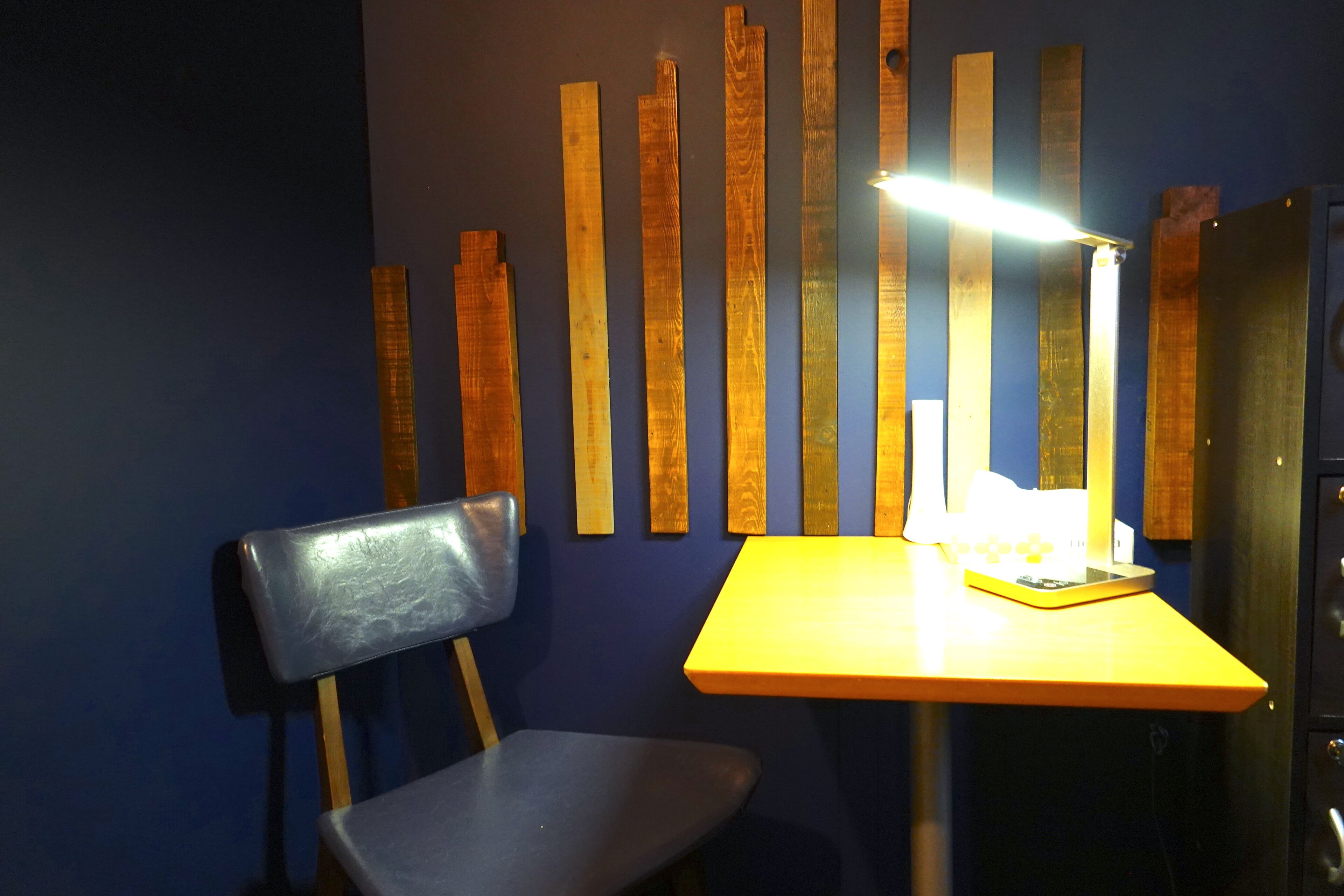 A room with a blue wall, a wooden panel design, a yellow table, and a black chair.