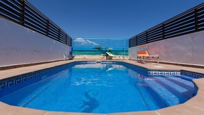 Une piscine avec vue sur l’océan, entourée d’une terrasse dotée de chaises longues et d’une rambarde.