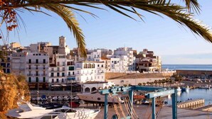 Un port de plaisance où sont amarrés des yachts, une ville côtière aux bâtiments blancs et un ciel dégagé.