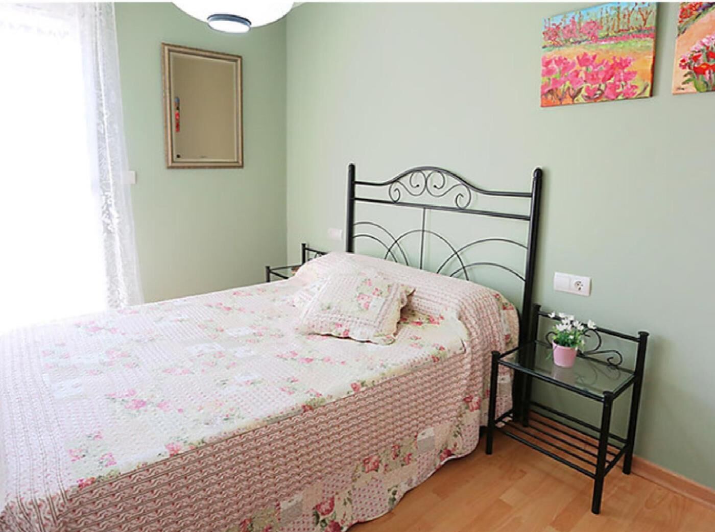 Un dormitorio con una cama, una mesita de noche, un espejo y dos cuadros en la pared.