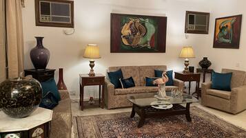Una sala de estar con un sofá, dos mesas auxiliares con lámparas, una mesa de centro, un jarrón grande y dos unidades de aire acondicionado fijadas a la pared.