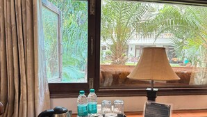 Une chambre d’hôtel avec vue sur les palmiers, une table avec une bouilloire, des bouteilles d’eau, des verres, un plateau et un petit panneau.