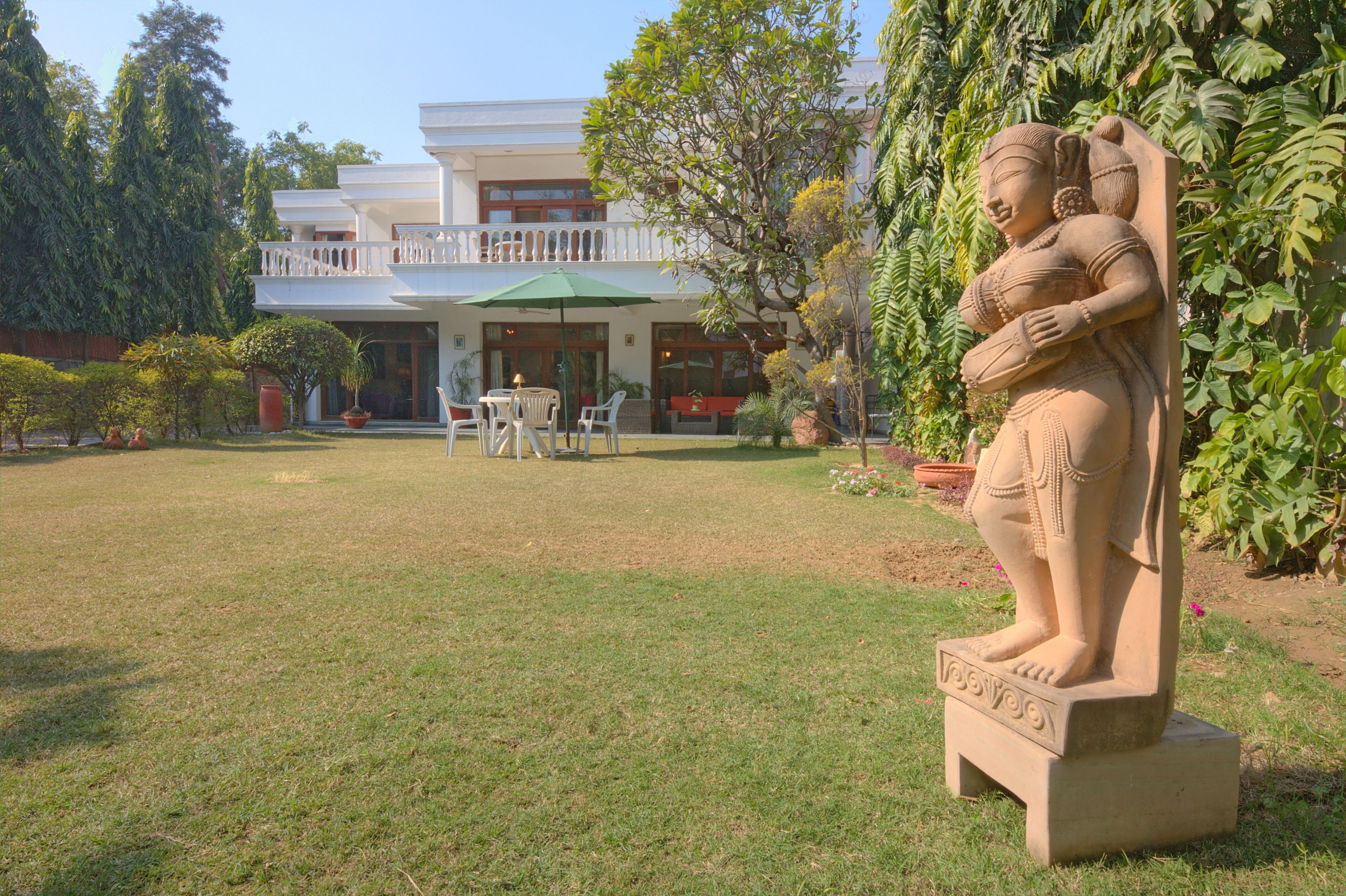 A statue in a garden with a building in the background.