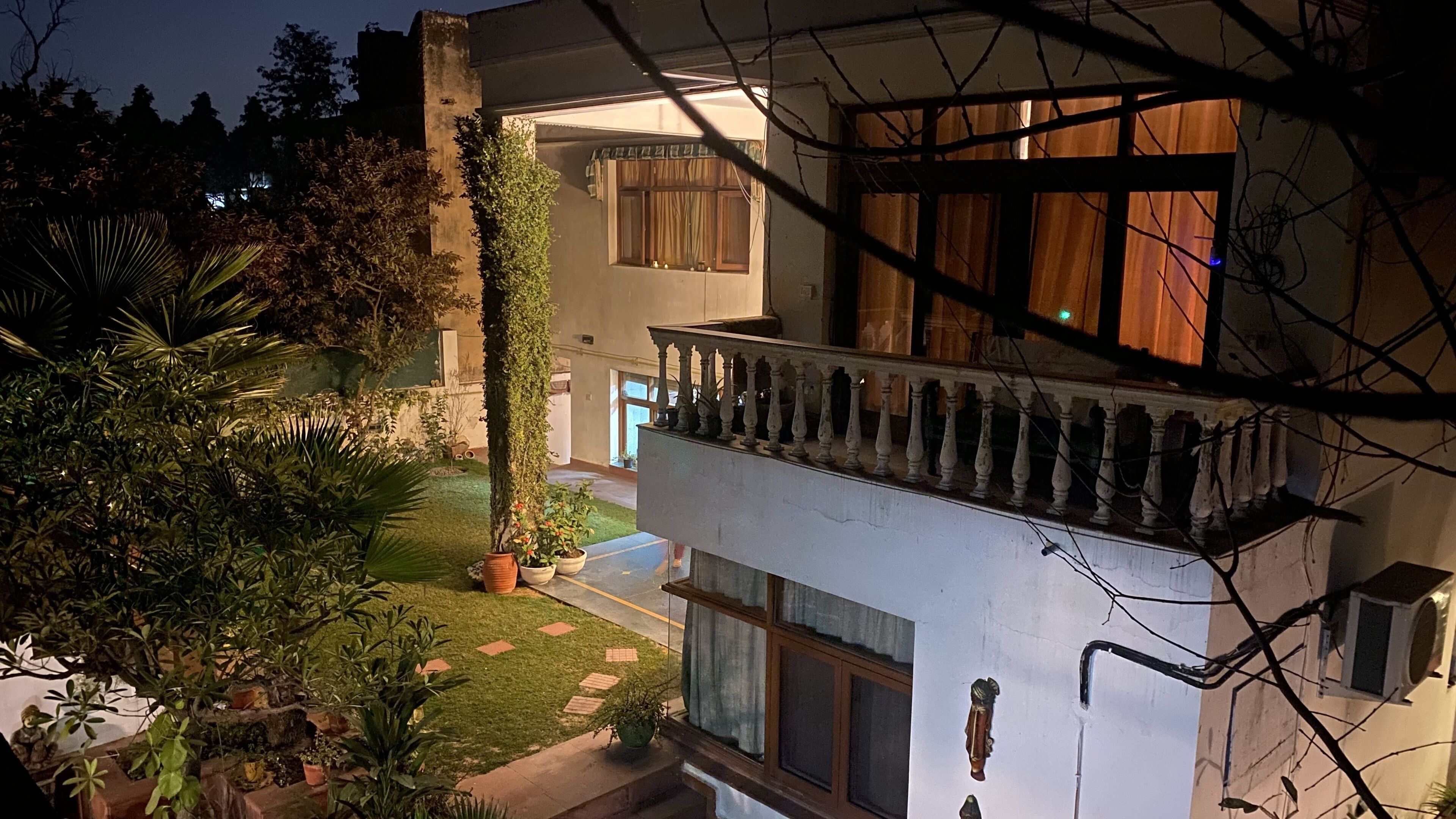 A multi-story building with a balcony, potted plants, and a well-maintained lawn.