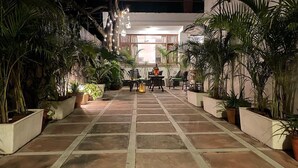 Une cour dallée, agrémentée de plantes en pot, avec une table et des chaises, et une lanterne.