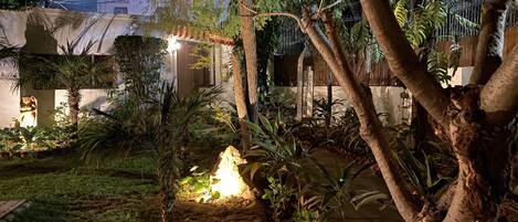 A garden with a fire pit, trees, and a building in the background.