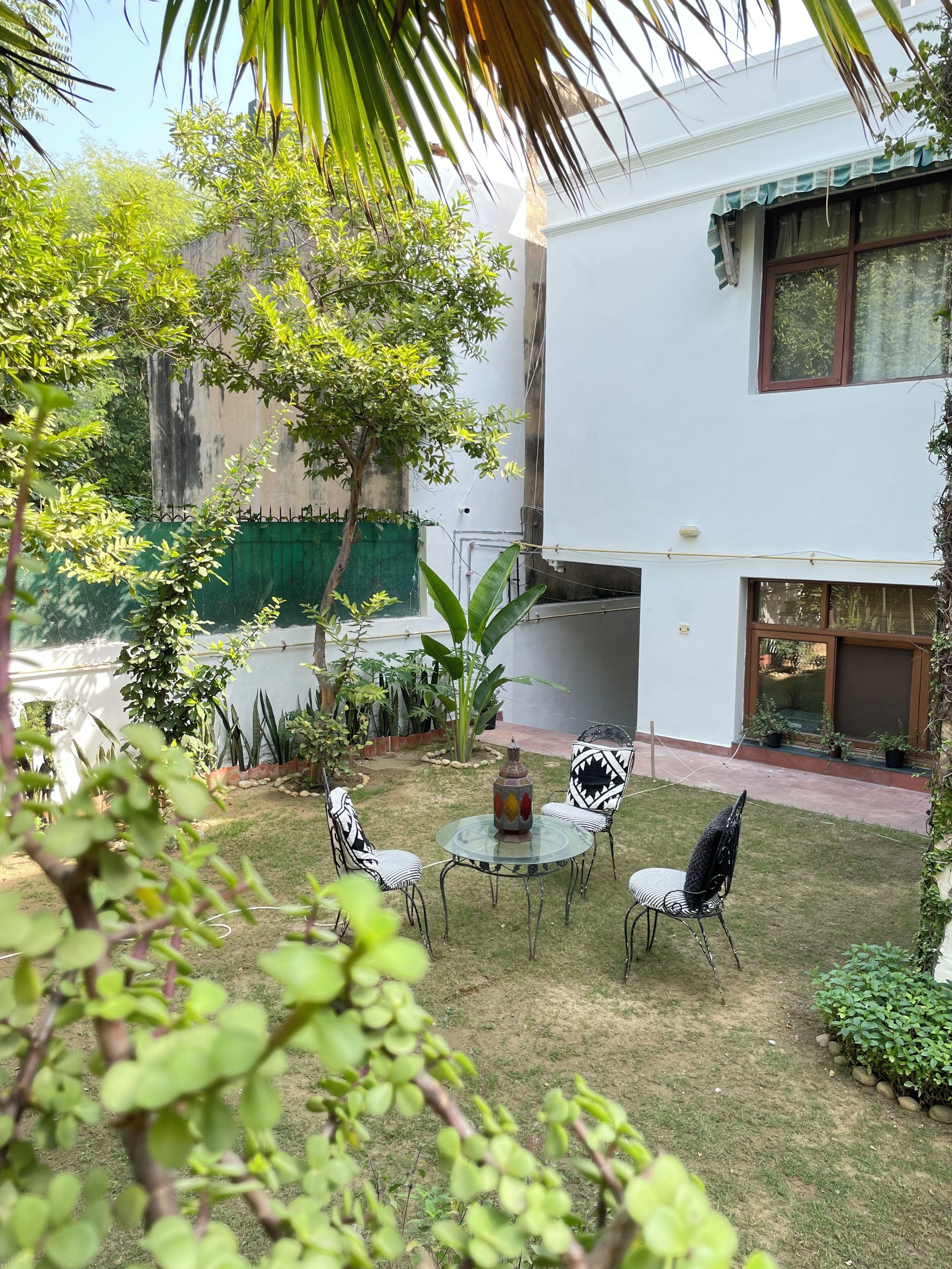 A courtyard with a round glass table, four chairs, and a decorative vase.