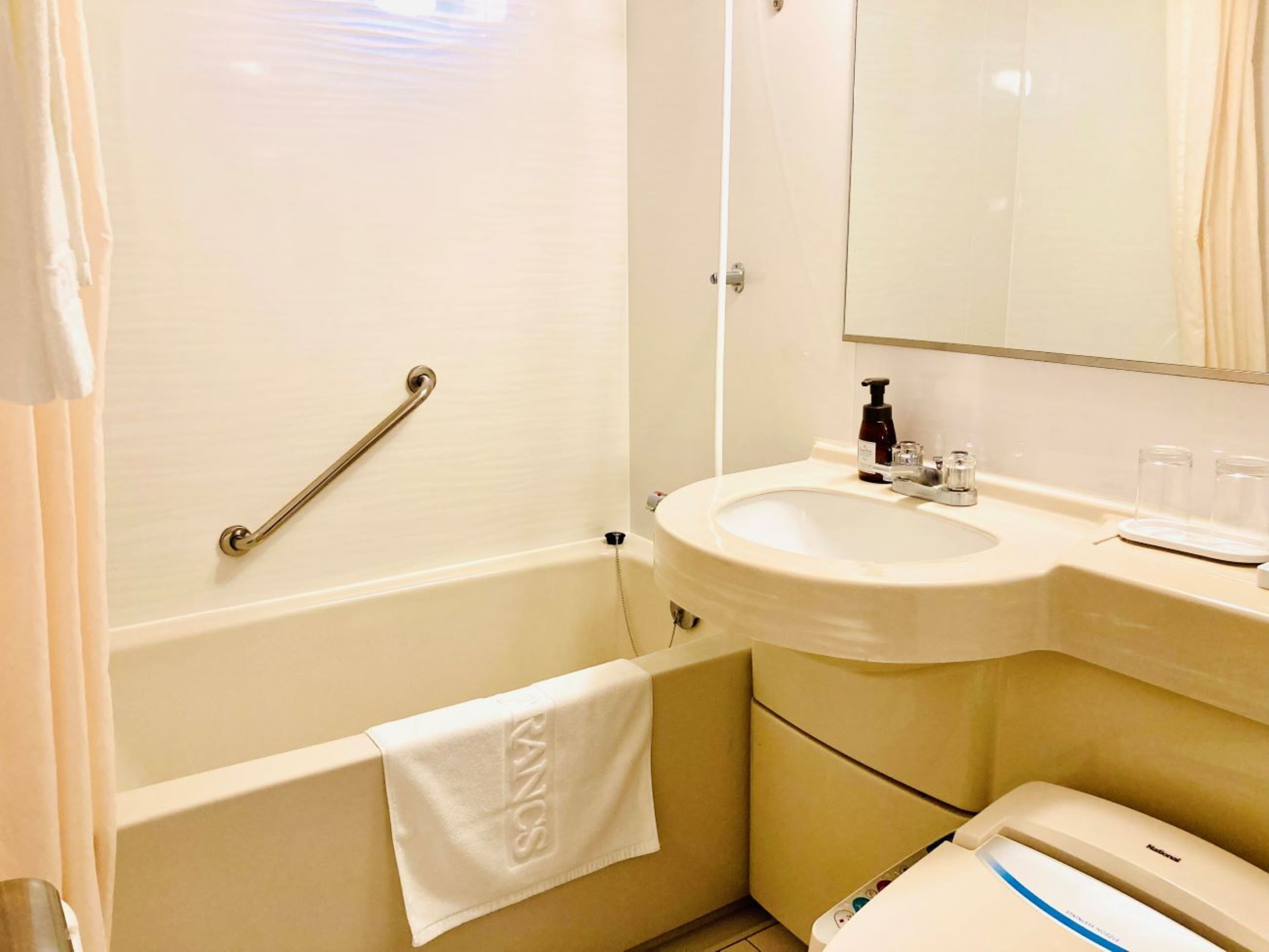 Un baño con bañera, lavamanos, espejo y toallero.