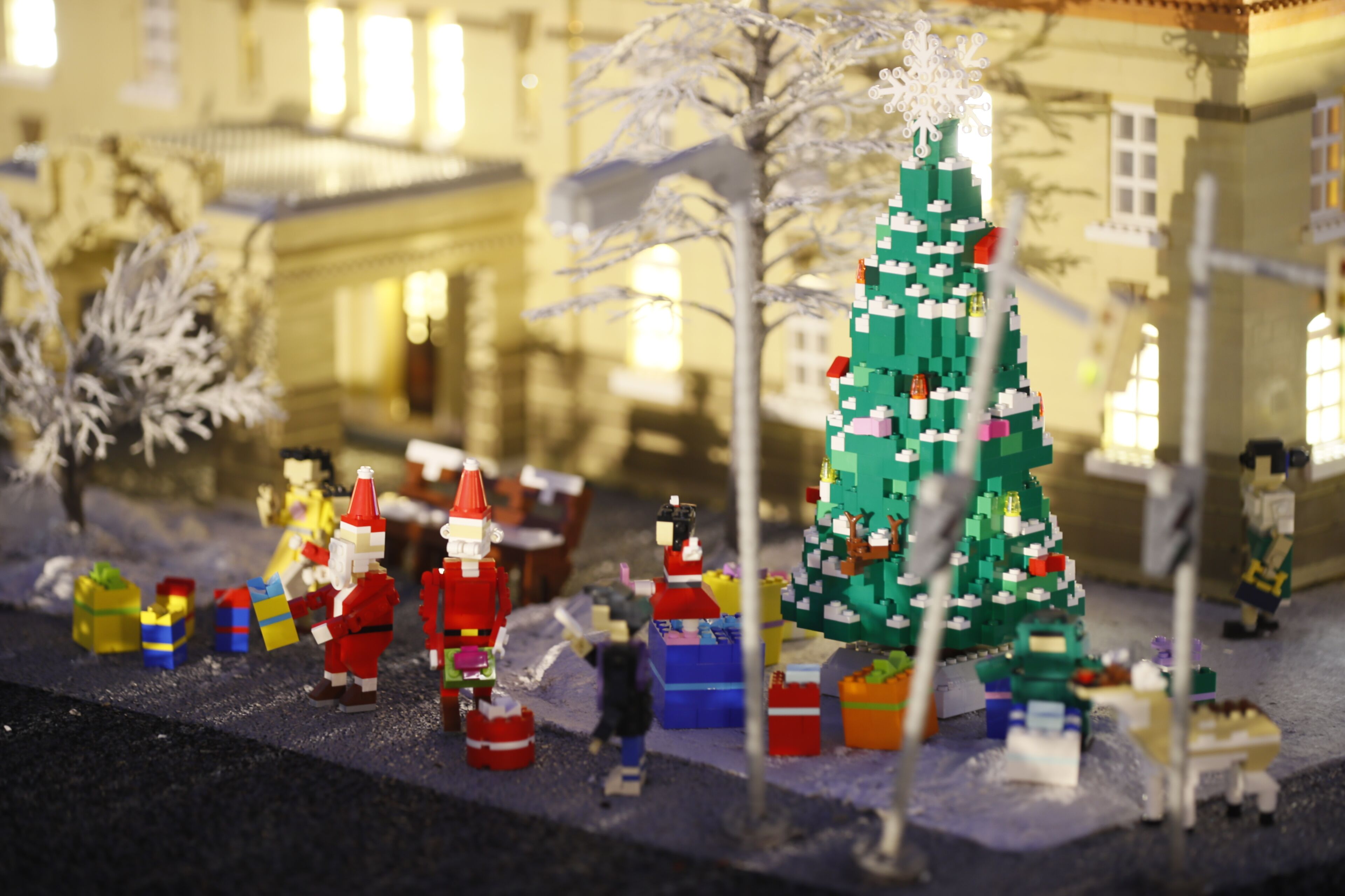 A LEGO scene with a large Christmas tree, figures of Santa Claus, and gift boxes.