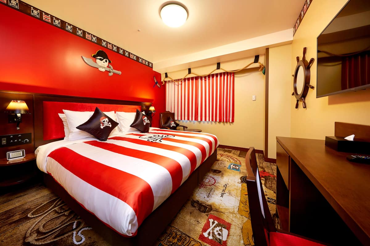 A hotel room with a large bed, a desk, a TV, and a window with striped curtains.