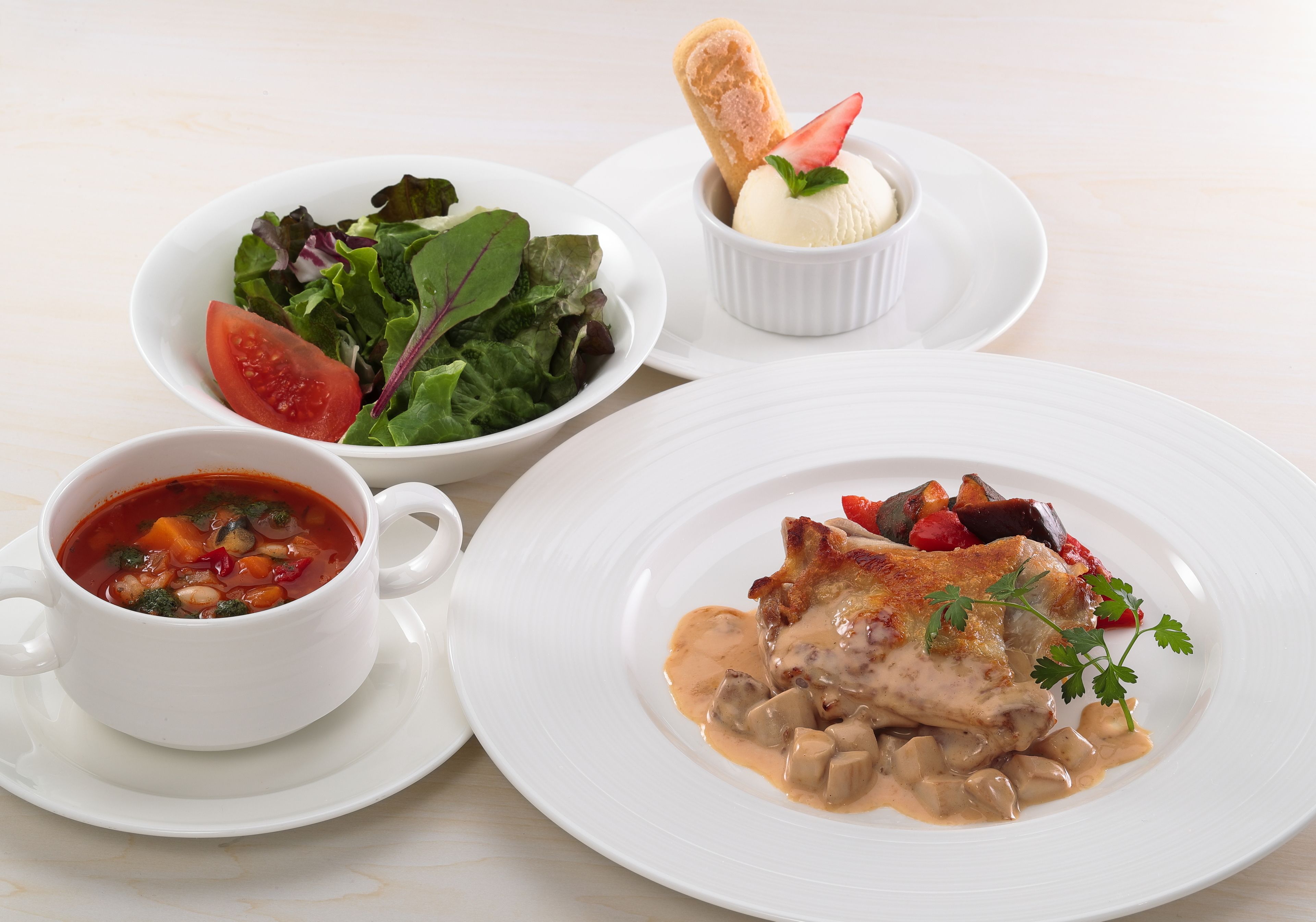 Une table avec trois plats : un bol de soupe, une assiette avec un morceau de viande et des légumes, et un saladier contenant une salade et une tranche de tomate.