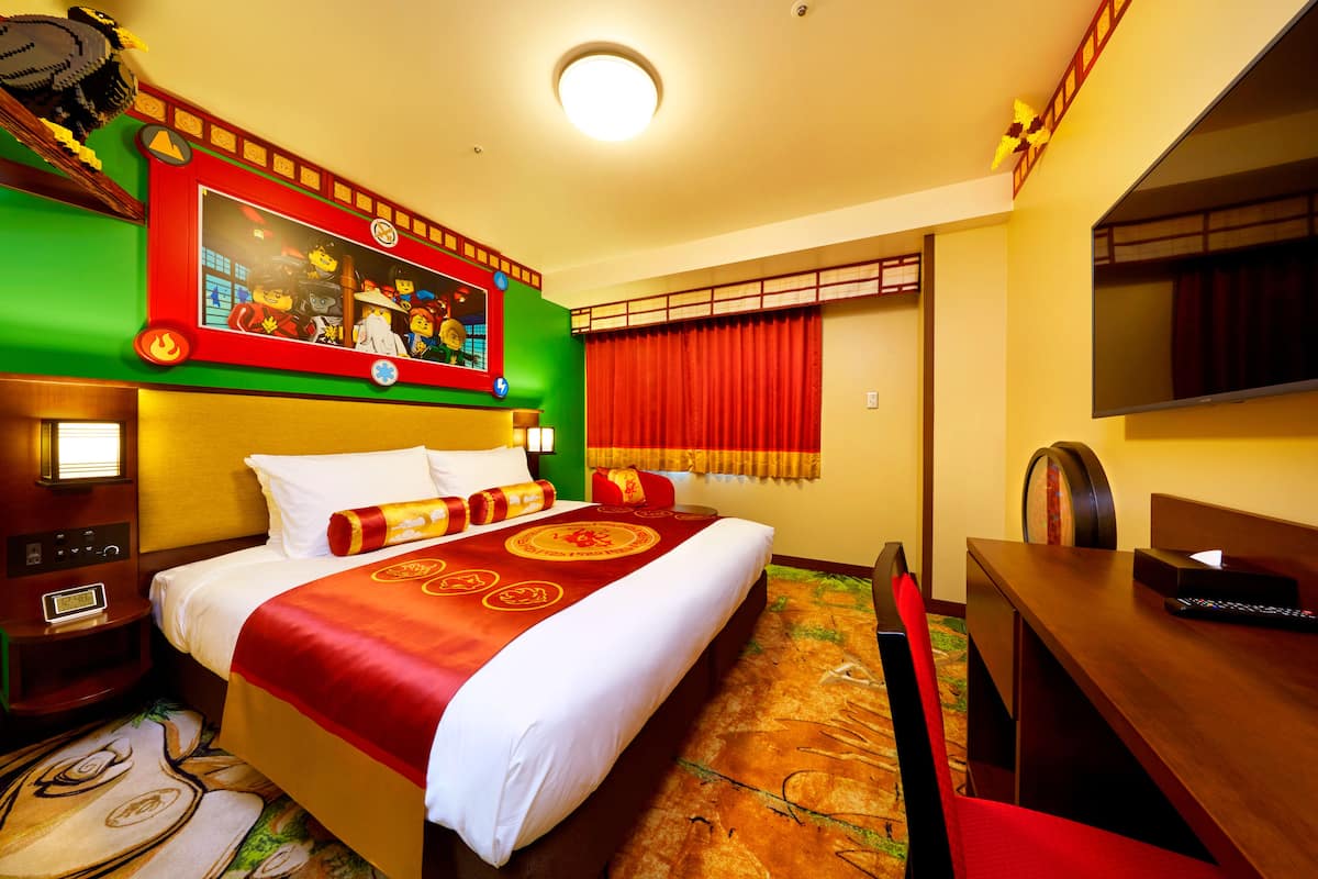 A hotel room with a large bed, a desk, a television, and a wall with a framed picture.